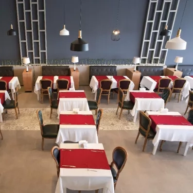 Une salle de restaurant intérieure avec des tables dressées de nappes rouges et blanches.