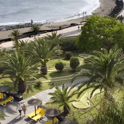 Une vue plongeante sur des jardins tropicaux luxuriants bordant une promenade et une plage.