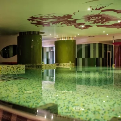 Une piscine intérieure élégante aux reflets verts, surplombée par un plafond décoré de motifs artistiques.