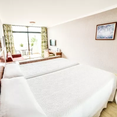 Une chambre lumineuse avec un grand lit double et une fenêtre donnant sur l'extérieur.