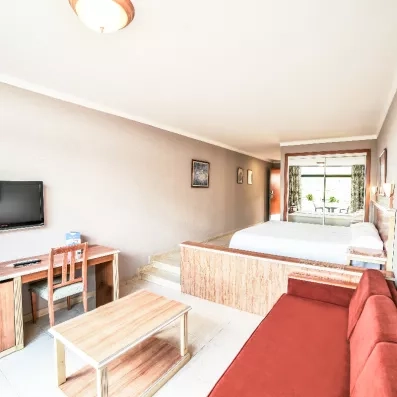 Un studio spacieux comprenant un coin salon avec canapé rouge et un espace nuit surélevé.