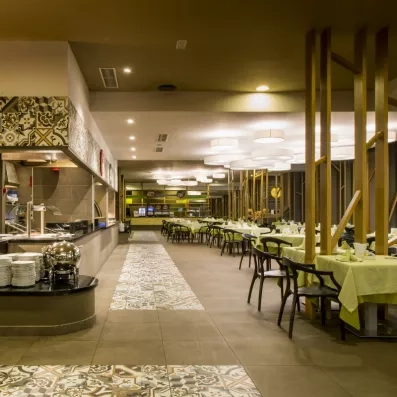 Une vaste salle de buffet lumineuse avec un long comptoir de service et de nombreuses tables nappées.