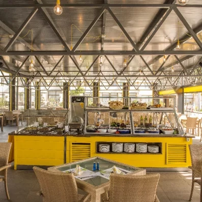 Un coin snack ou buffet extérieur sous une structure métallique industrielle avec un comptoir jaune vif.