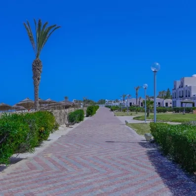 Allée pavée bordée de jardins et de lampadaires menant vers la plage de sable fin à Djerba.