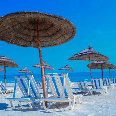 Transats blancs et parasols en paille sur la plage privée de sable fin de Djerba.