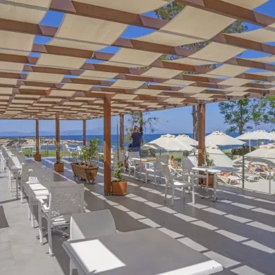 Un espace de restauration extérieur abrité par une pergola, offrant une vue sur la mer.
