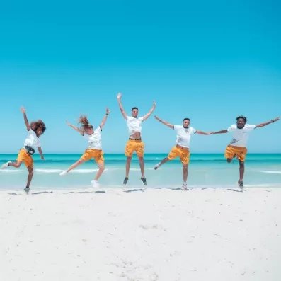 Équipe d'animation dynamique sautant de joie sur la plage de sable blanc du Vincci Dar Midoun.
