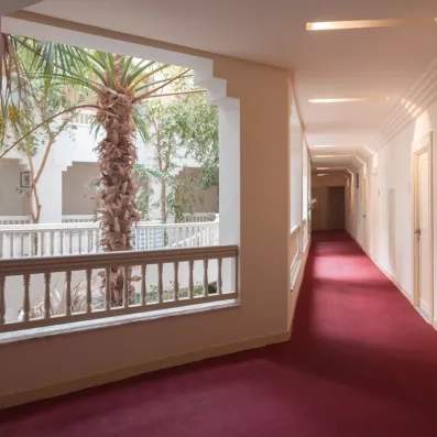 Couloir lumineux avec moquette rouge et vue sur le patio arboré du Vincci Dar Midoun, Tunisie.