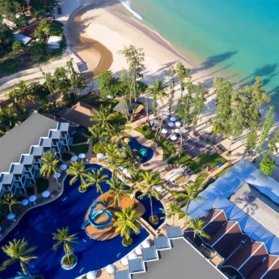 Une vue aérienne d’un complexe hôtelier, situé entre une piscine et une plage aux eaux turquoise.