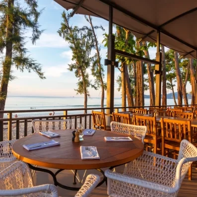 Une table dressée sur une terrasse couverte, prête pour un dîner face au coucher du soleil.