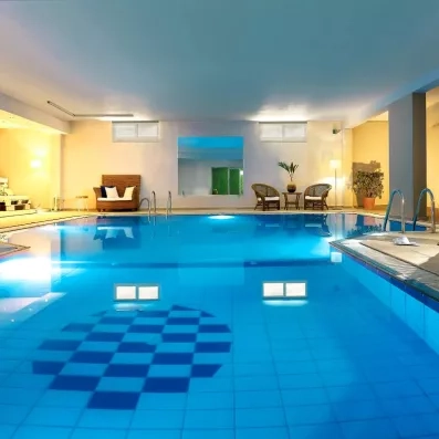 piscine intérieure, deux fauteuils au bord avec une petite table et une plante posée dessus, un canapé, un grand miroir, lumineux