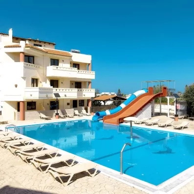 piscine de l'hôtel avec deux toboggans un couvert bleu et blanc et un orange découvert, ciel bleu sans un nuage, transats, bâtiment crétois