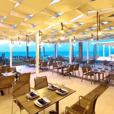 restaurant de la plage, tables carrées en bois, chaises marrons, luminaires en cordes, vue mer