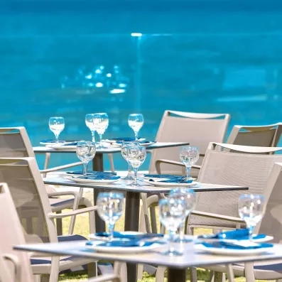 tables carrées, chaises beiges, verres, terrasse avec vue sur la mer