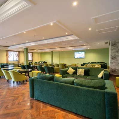 café maure de l'hôtel avec des canapés vert foncé, chaises et tables pour s'installer devant la télé au fond dur le mur