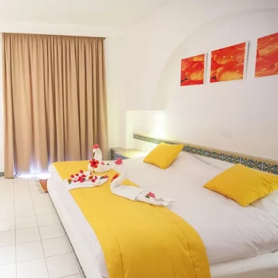 Suite lumineuse du Seabel Aladin avec décoration romantique en serviettes, rideaux beiges et touches de jaune soleil.