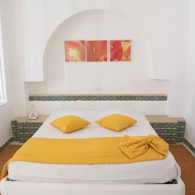 Chambre double de l'hôtel Seabel Aladin Djerba avec décoration typique, carrelage artisanal bleu et jaune, et jeté de lit jaune vif.
