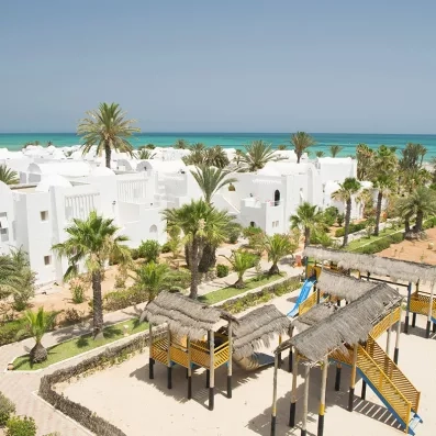 Vue panoramique des bungalows blancs de style manceaux du Seabel Aladin Djerba bordant la mer Méditerranée et aire de jeux pour enfants.