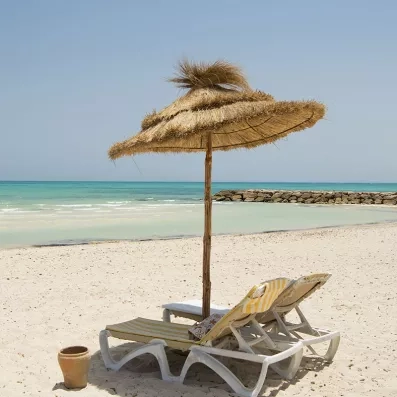 Transats et parasols en paille sur la plage paradisiaque du Mondi Club Seabel Aladin à Djerba.