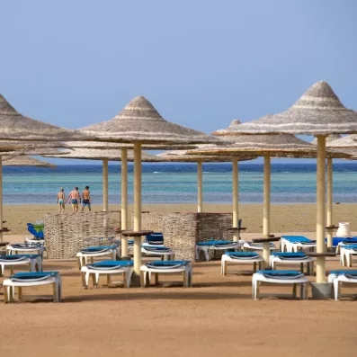 Parasols en paille et transats sur la plage privée du Stella Beach face à la Mer Rouge.
