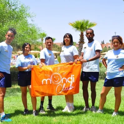 équipe d'animation avec une tenue uniforme, portant le drapeau de mondi club dans le jardin de l'hôtel