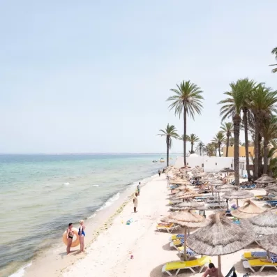 Plage de sable fin bordée de palmiers et parasols en paille au Mondi Club Shems Monastir.