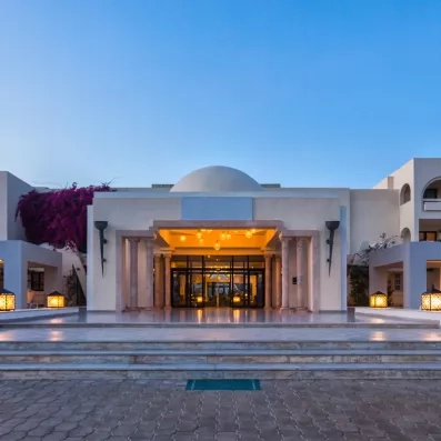 Entrée principale illuminée du Djerba Aqua Resort avec architecture traditionnelle, dôme blanc et lanternes au crépuscule.