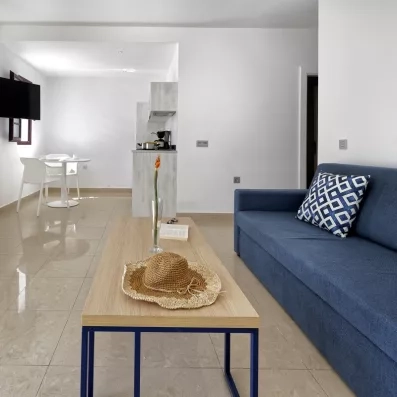 Un salon d'appartement avec un canapé et une table basse en bois, s'ouvrant sur une cuisine américaine.