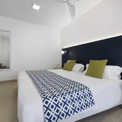 Une chambre d'hôtel lumineuse, avec un grand lit blanc souligné par un chemin de lit.