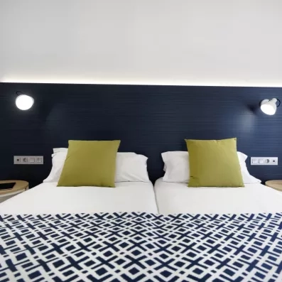 Un gros plan sur la tête de lit bleu marine, avec des coussins et des liseuses modernes de chaque côté.