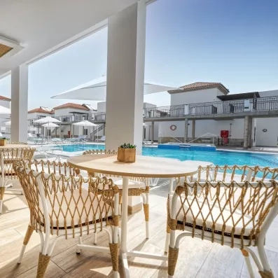 Une terrasse de restaurant ensoleillée avec des chaises en osier offrant une vue sur une piscine.