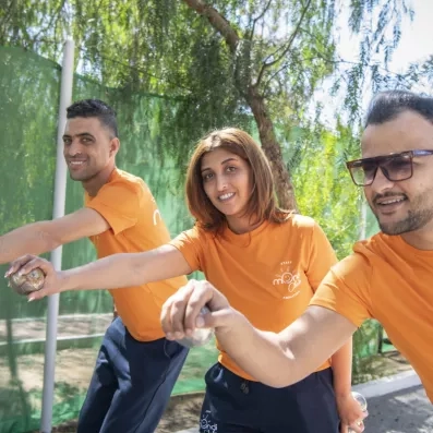 Animateurs en tenue orange jouant à la pétanque sous les arbres au Mondi Club Shems Monastir.