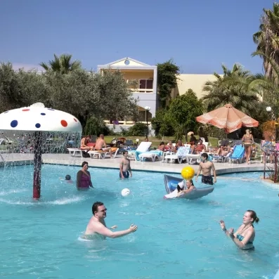 piscine avec fontaine champignons et des gens qui bronzent et jouent au ballon