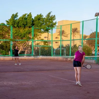 cours de tennis en terre battue, deux personnes qui jouent, bâtiment de l'hôtel