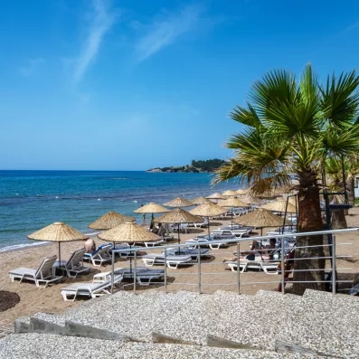 Une plage de sable fin aménagée de nombreux parasols en paille et palmiers.