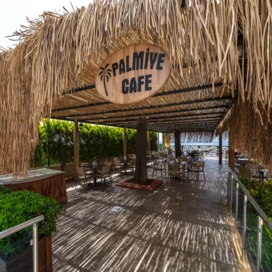 Un restaurant sous un toit en chaume, avec des tables en bois et un chemin menant vers la mer.