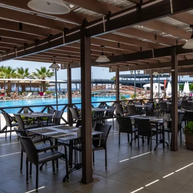 Un restaurant extérieur au bord d'une piscine avec des tables et chaises sous des pergolas.