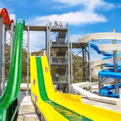 pusieurs toboggans jaune et vert, personnes qui glissent dans l'aquapark, maitre nageur en haut de la structure, ciel bleu avec des nuages