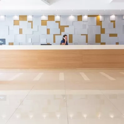 L'accueil et la réception de l'hôtel sol unis en beige et comptoir en bois avec la réceptionniste au téléphone 