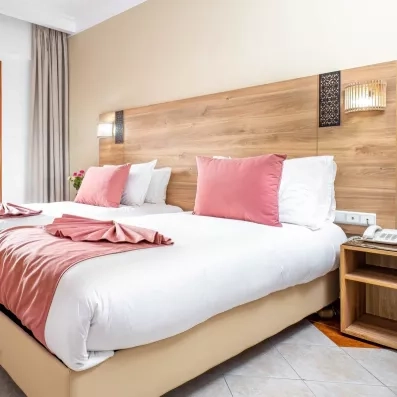 Chambre de l'hôtel avec deux lits collé en blanc et rose poudré et tête de lit en bois