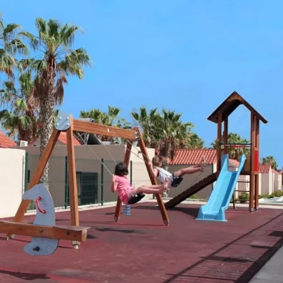 Une aire de jeux extérieure sécurisée avec des balançoires et un toboggan sous le soleil.