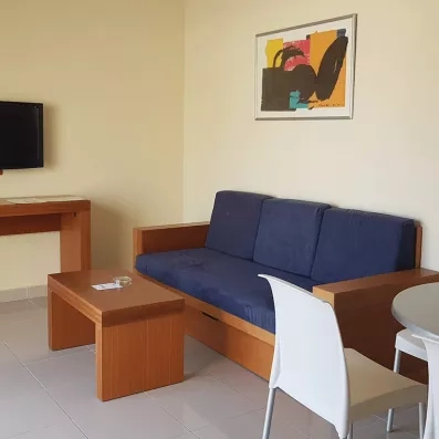 Un coin salon sobre comprenant un canapé, une table basse en bois et une télévision murale.