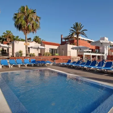 Une grande piscine bleue entourée de nombreux transats parsemé de palmiers.