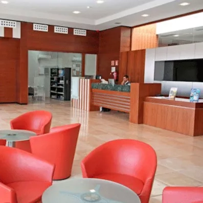 Un hall d'accueil moderne et lumineux avec un comptoir en bois et des fauteuils rouges arrondis.