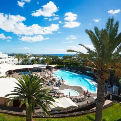 Une vue montre une grande piscine d'hôtel entourée de palmiers et de transats.