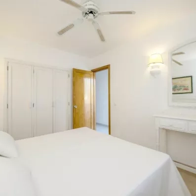 Un plan large d'une chambre avec un lit double, une commode et une porte entrouverte.