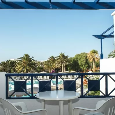 Un balcon aménagé avec une table et des chaises, offrant une vue sur les palmiers.