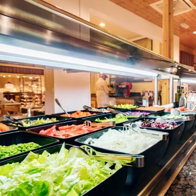 Un buffet de salades propose une variété de légumes frais, sous un éclairage suspendu.