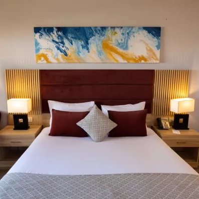 Lit king-size, tête de lit bordeaux et œuvre d'art moderne au Stella Beach Resort, Hurghada, Égypte.