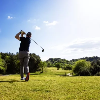 Un golfeur en plein mouvement sur un parcours verdoyant sous un ciel bleu.